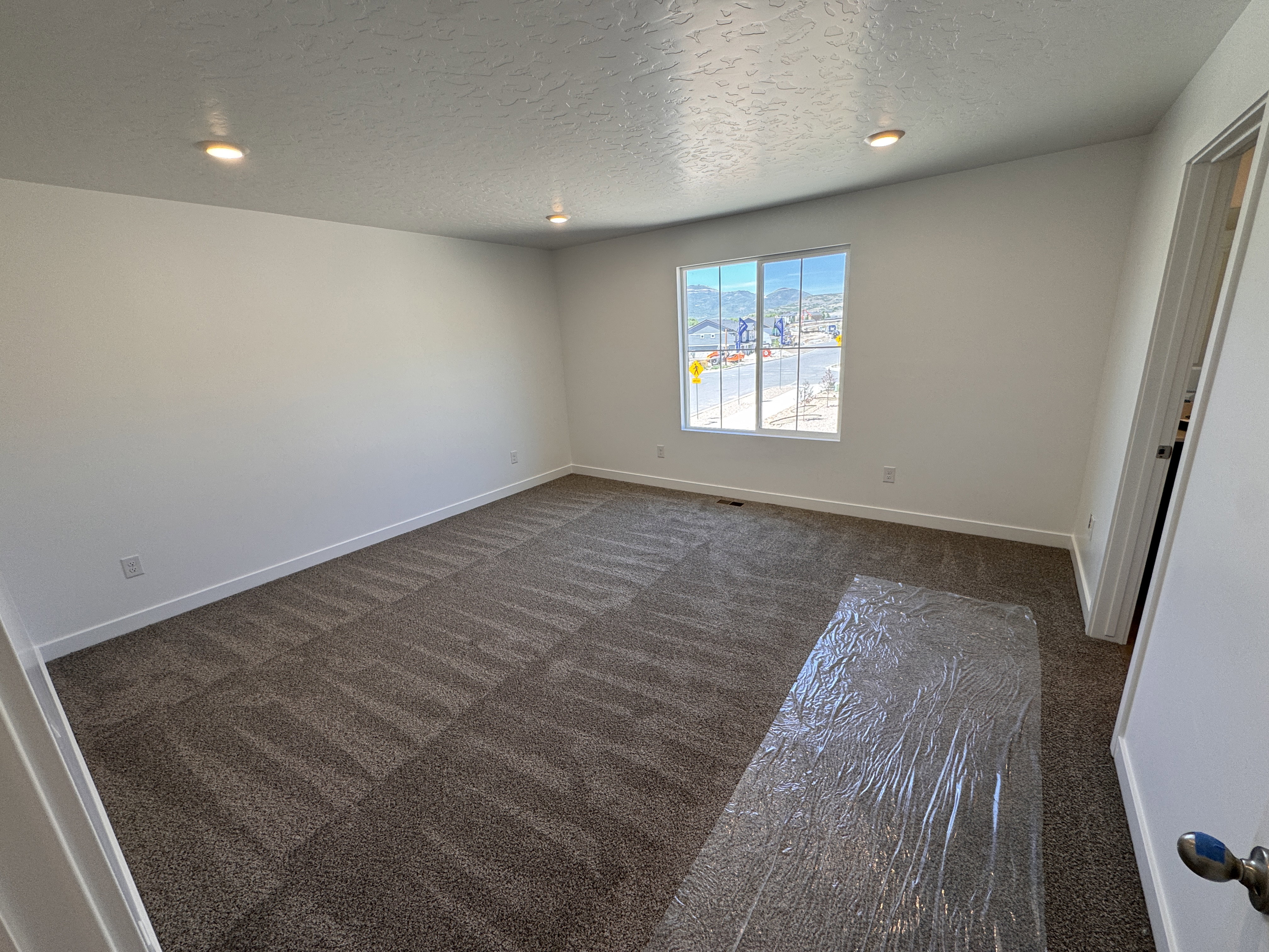 Spacious room with recessed lighting, neutral tone carpeting, white walls, and a large window offering natural light