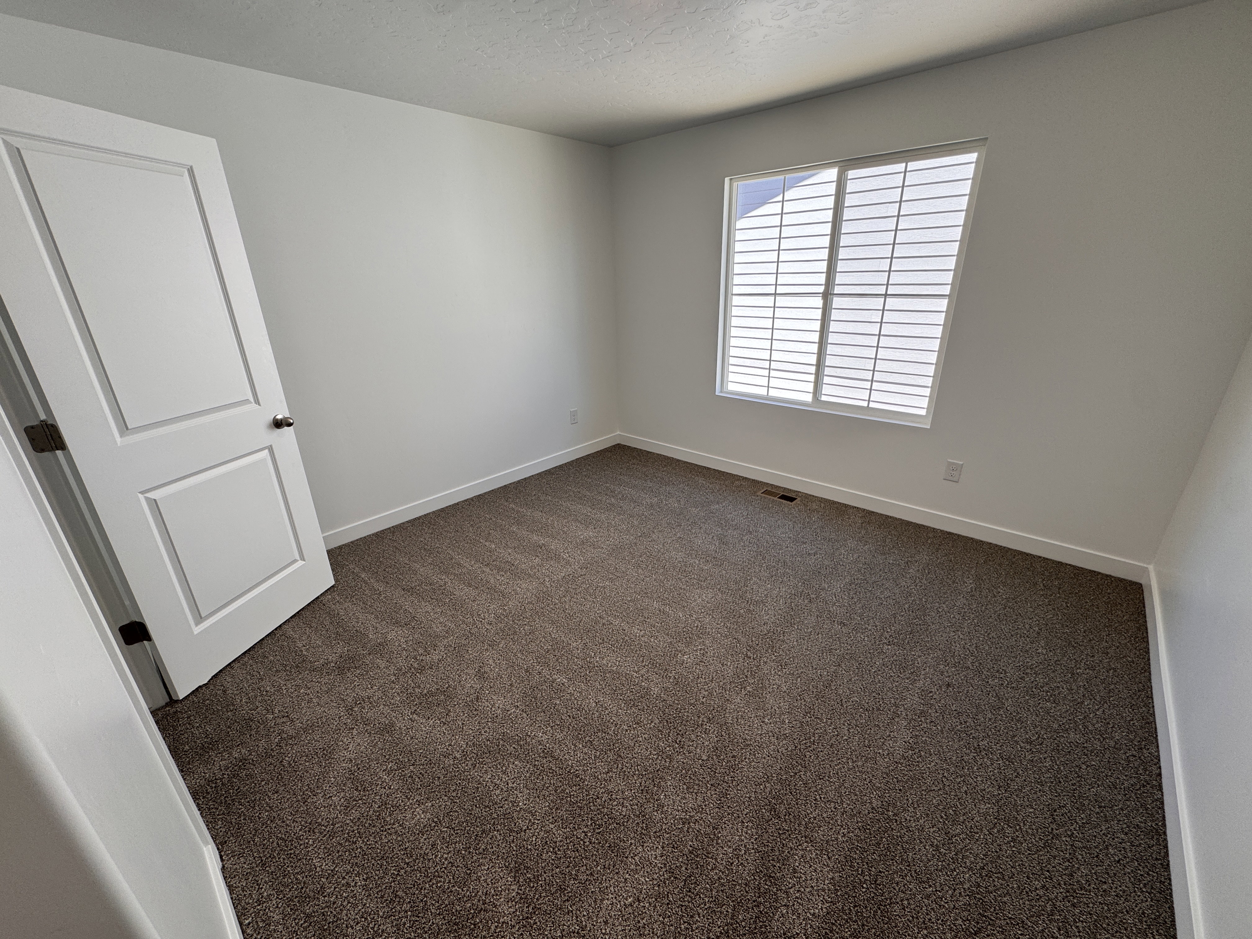 Neutral tone wall paint with white trim, brown carpeting, and a white window with horizontal blinds