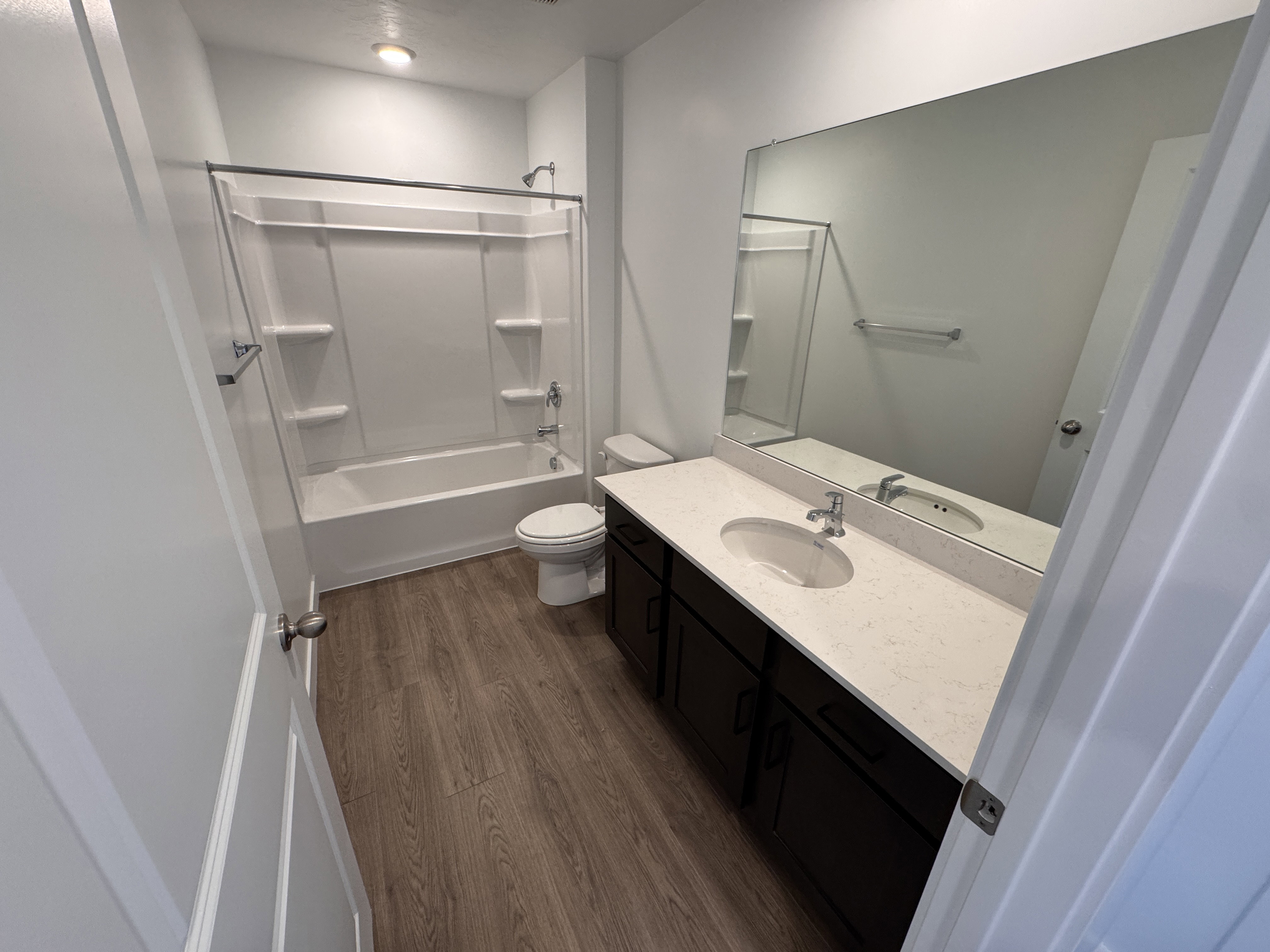 Full bathroom featuring a white tub/shower combination, dark wood vanity with white countertop, integrated sink, and a large wall-mounted mirror