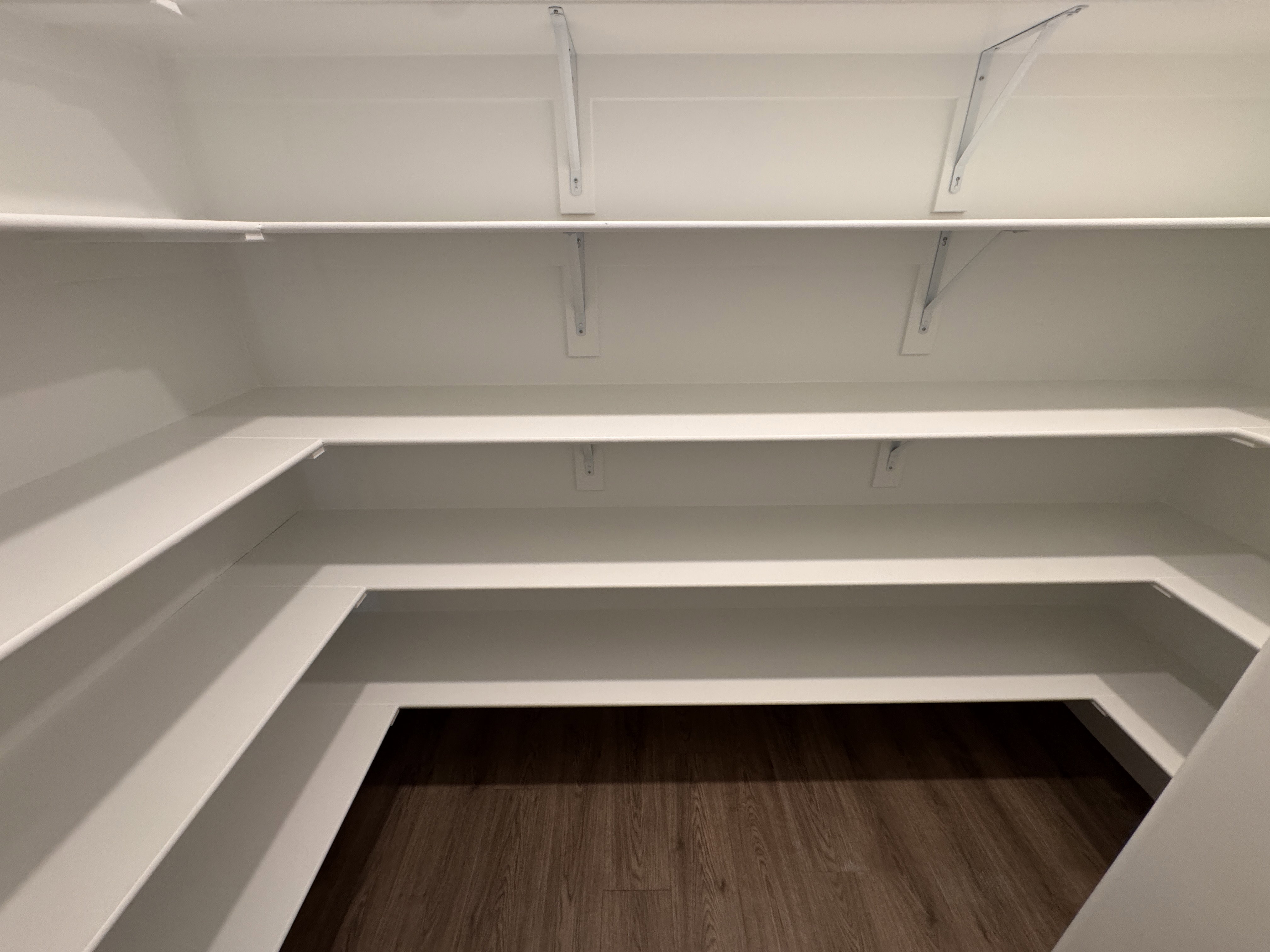 Spacious walk-in pantry featuring white shelving, multiple storage levels, and wood-finish flooring