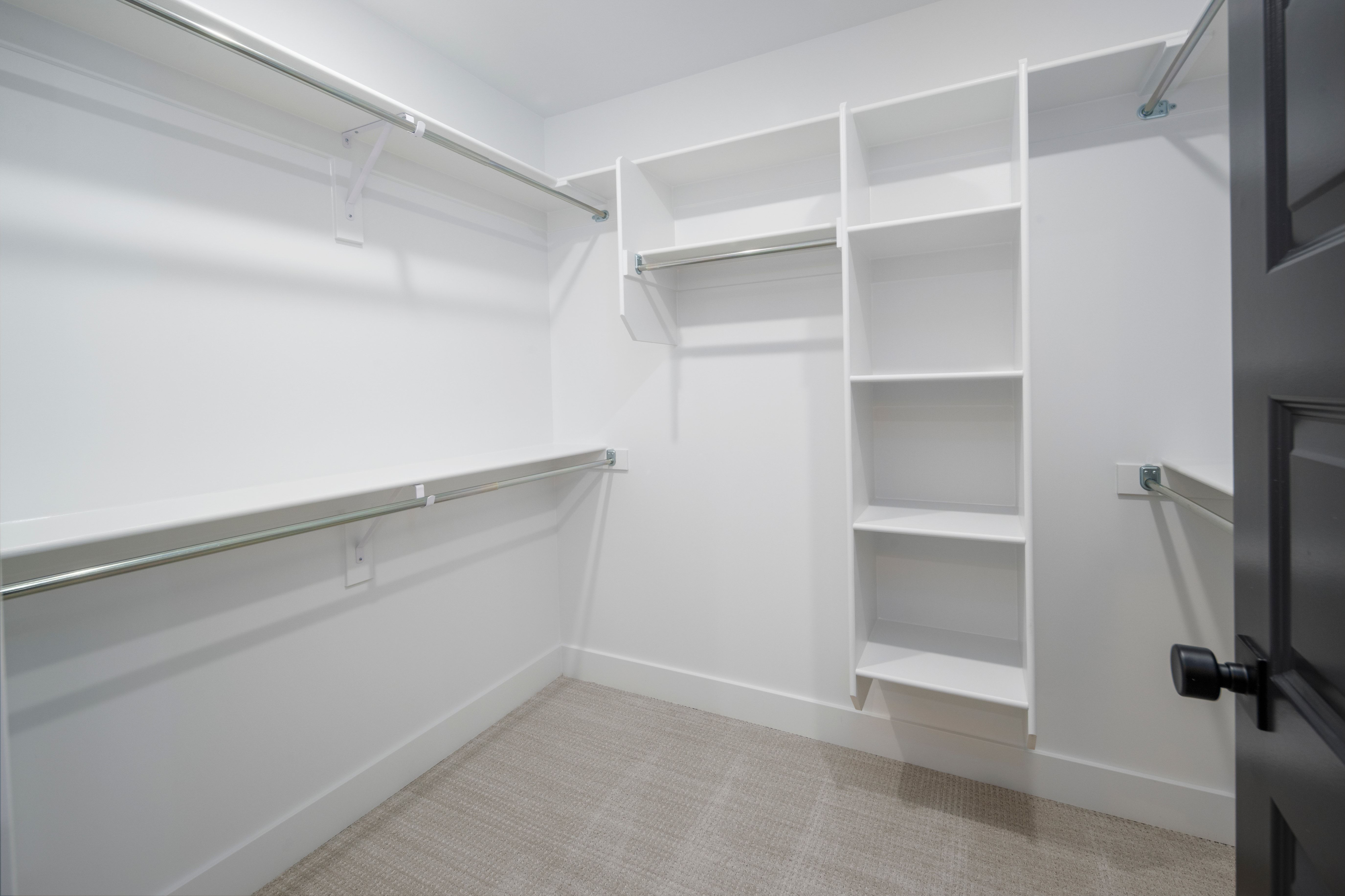 Walk-in closet with white shelving, multiple hanging rods, and light-toned carpet flooring