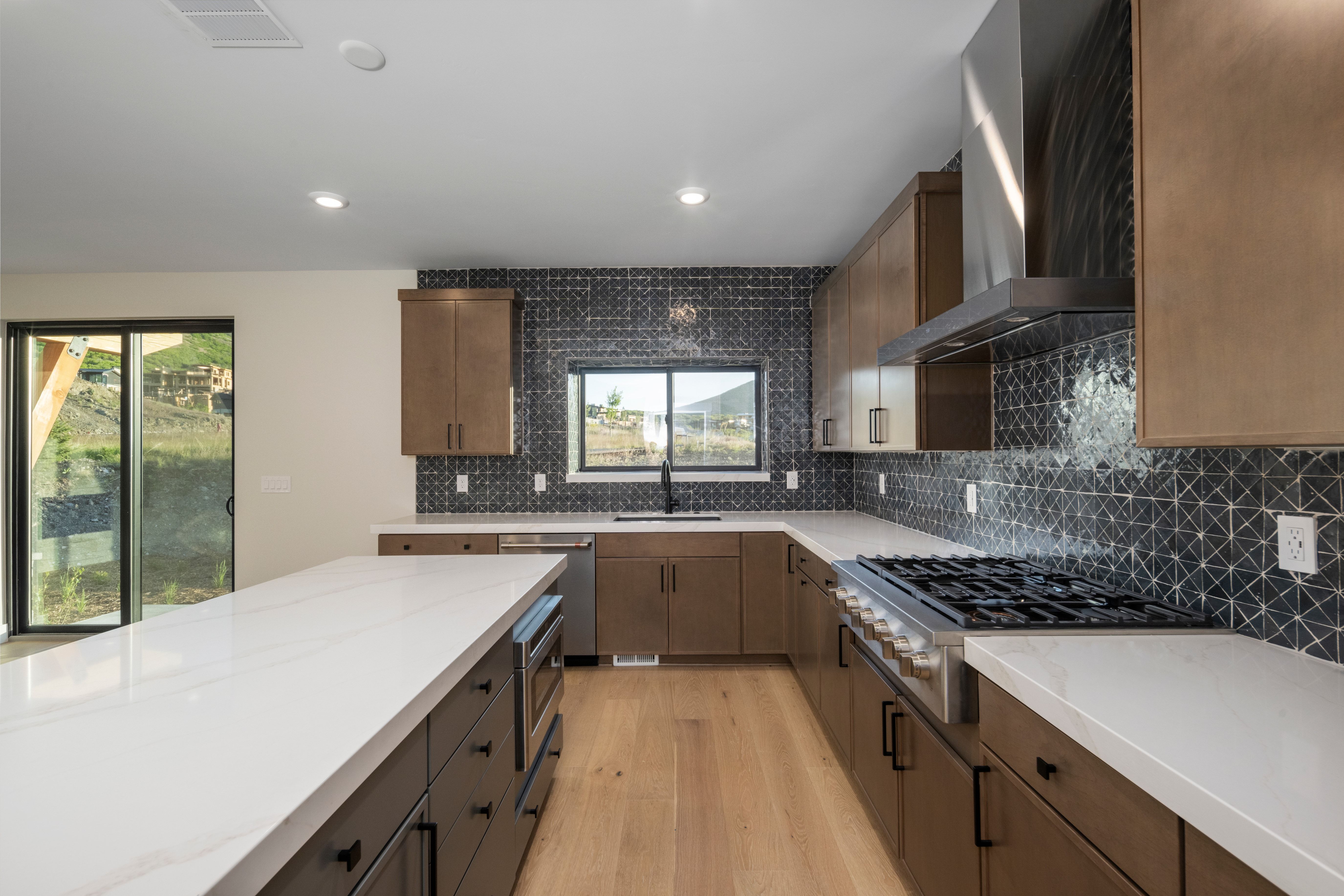 Gourmet kitchen featuring a substantial island with stone countertops, a full-height geometric tile backsplash, and wood-finish flooring