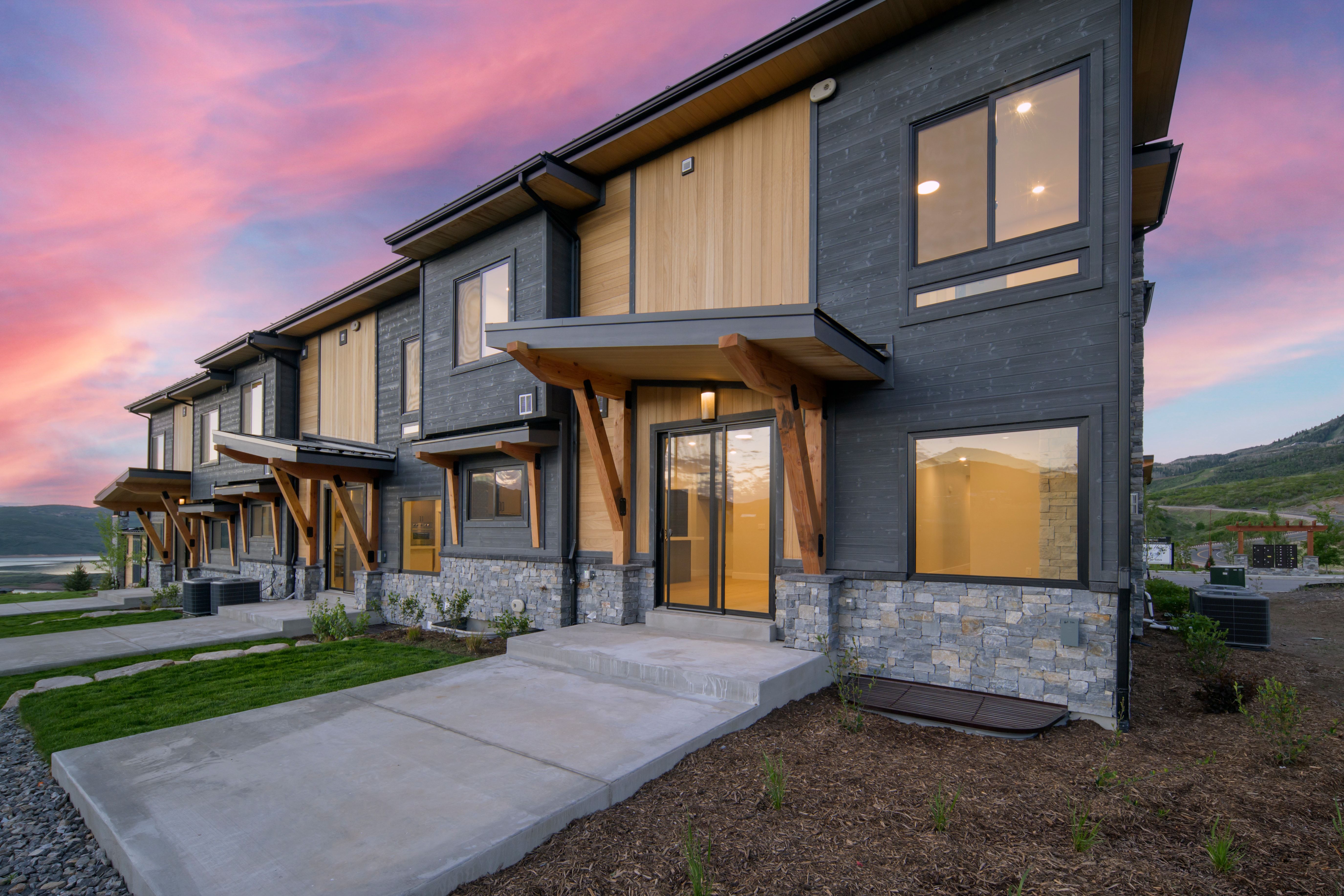 Modern townhome exteriors featuring dark siding, natural wood accents, and stone veneer foundations