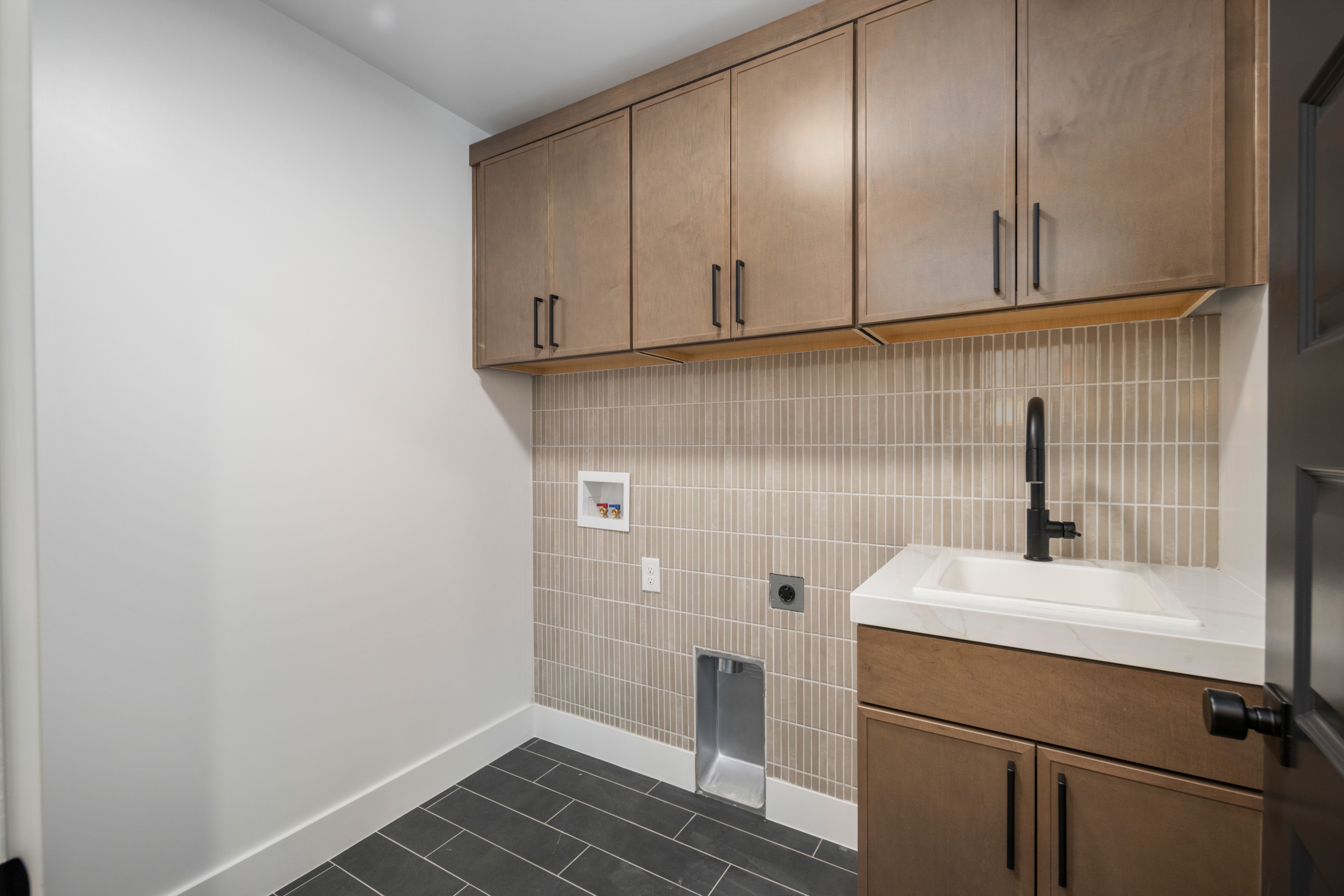 Laundry area featuring wood-finish cabinetry with matte black hardware