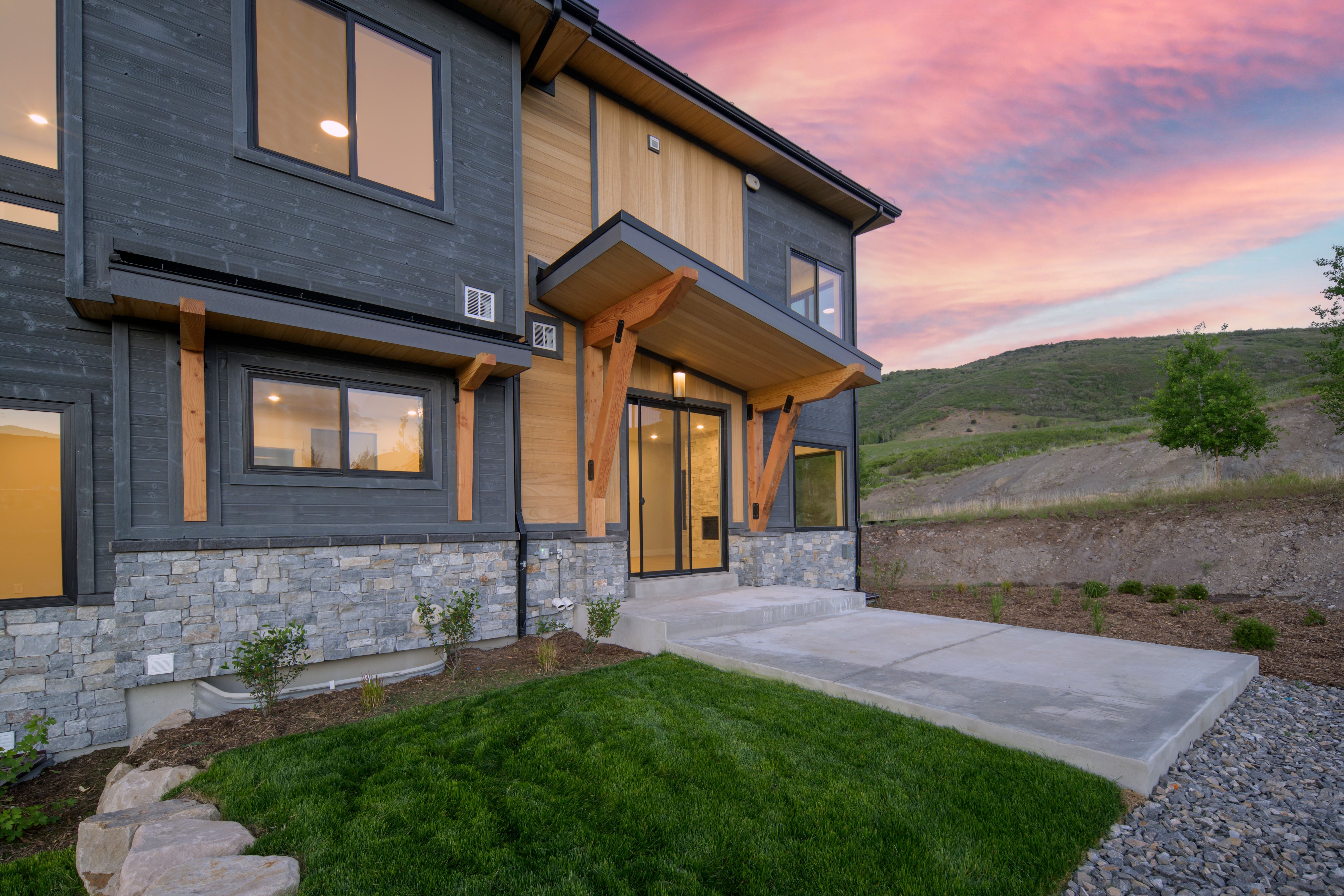 Contemporary architectural facade featuring dark horizontal siding, light wood-tone accents, and stone veneer foundation