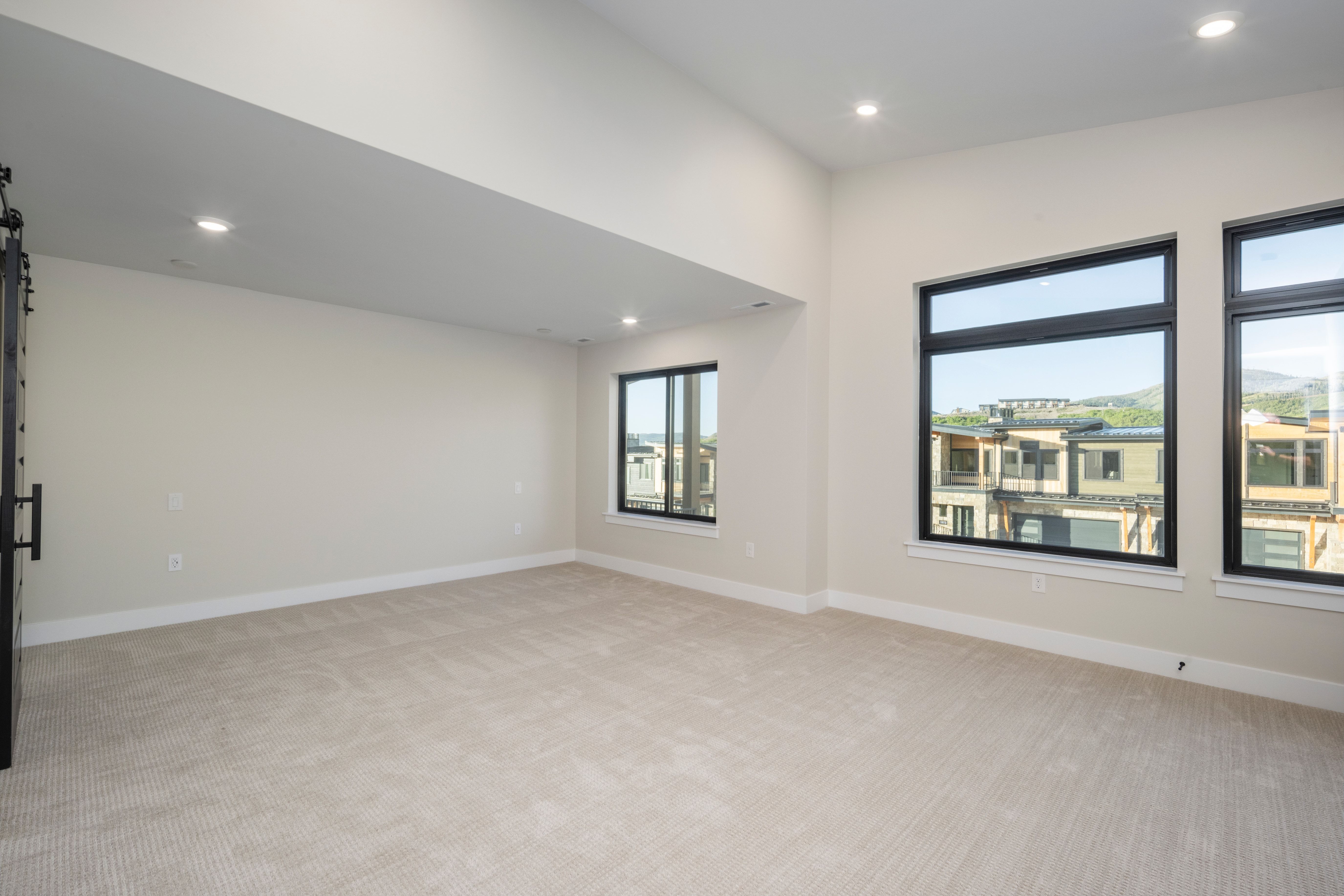 Spacious interior room featuring light-toned carpeting, recessed lighting, and expansive windows