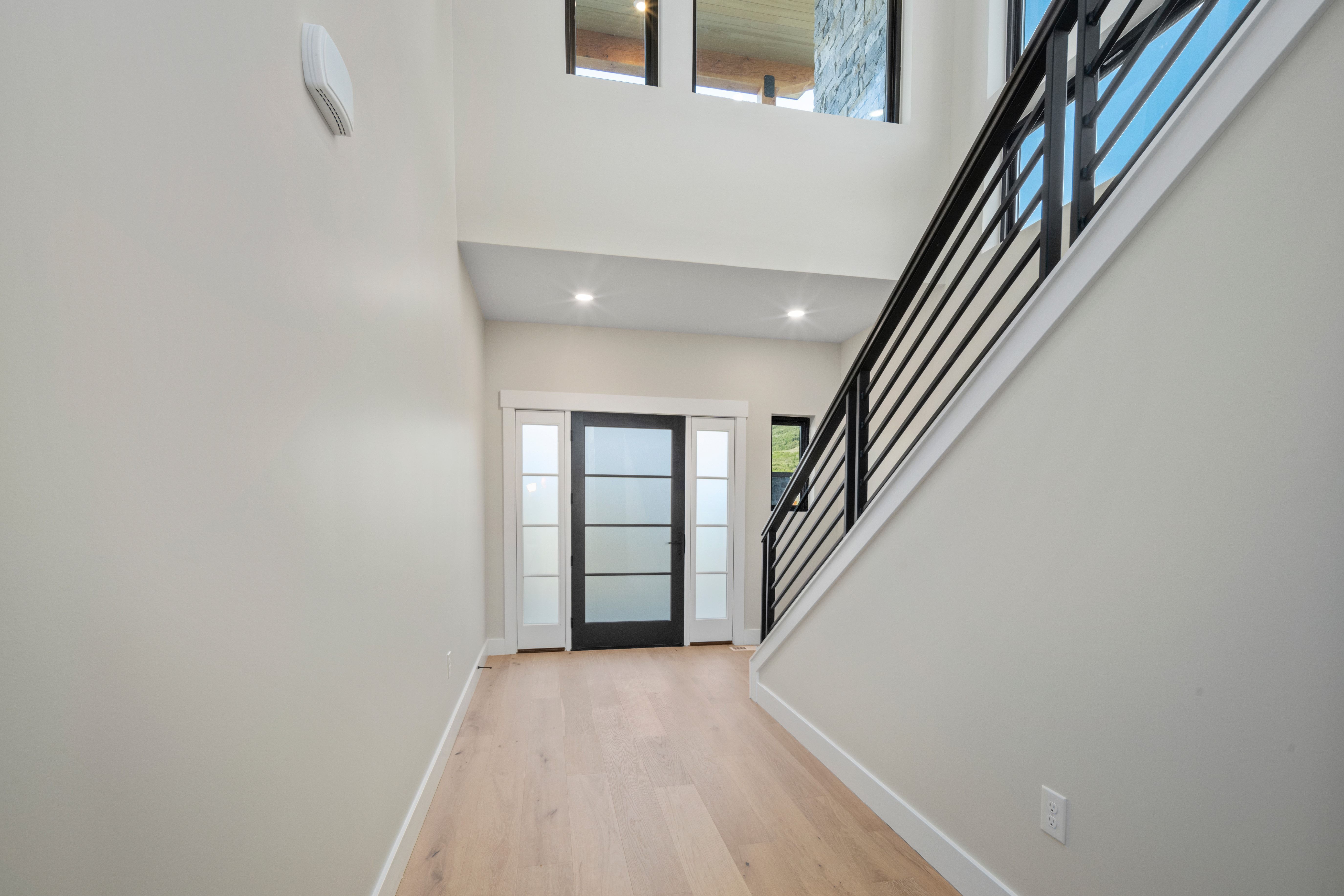 Contemporary entryway featuring light wood-finish flooring, a modern black metal staircase railing, and recessed lighting