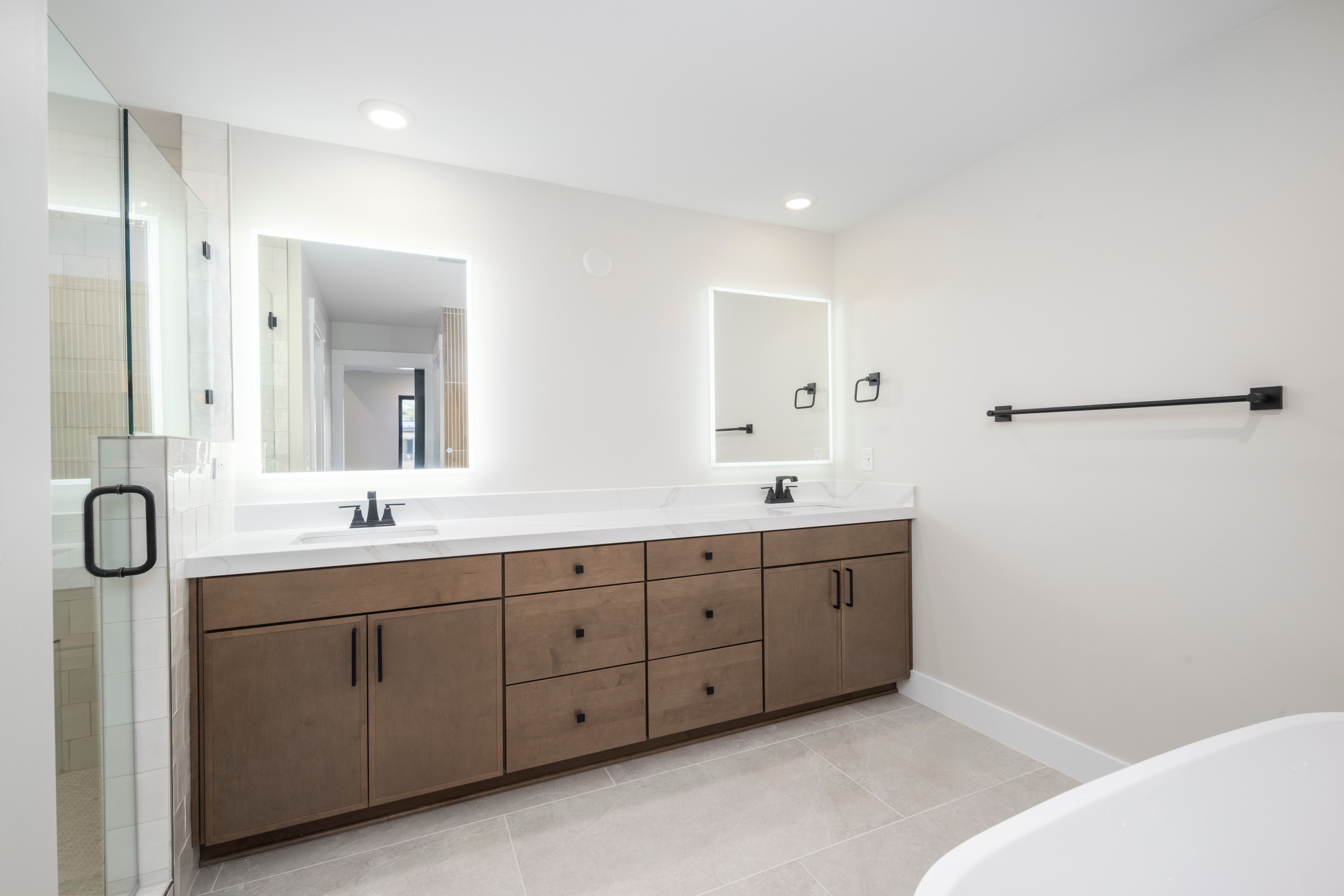 Double vanity featuring wood-finish cabinetry, white countertops, and backlit mirrors