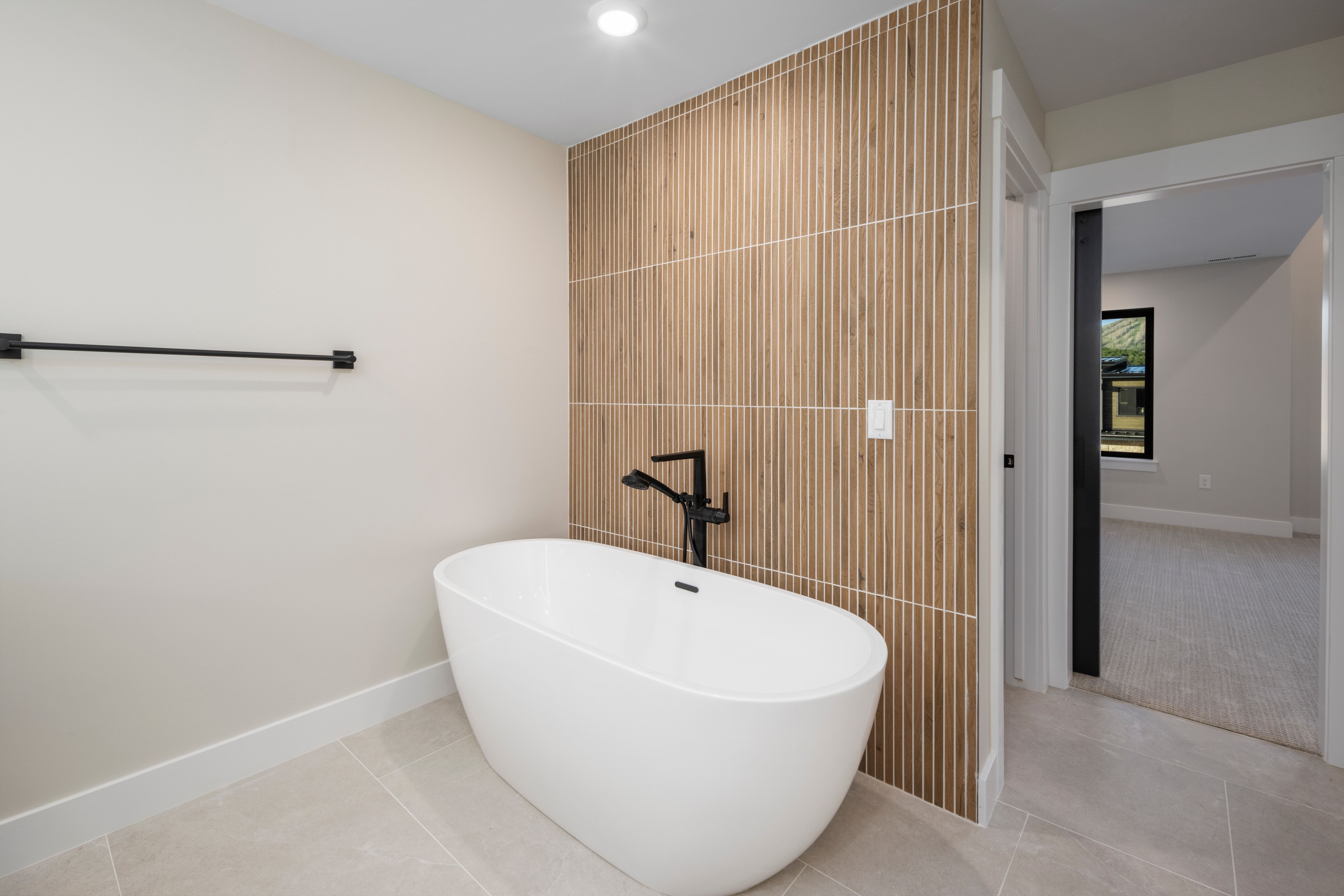 Freestanding soaking tub with matte black floor-mounted faucet, complemented by a ribbed wood-finish accent wall