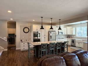 Open-concept kitchen featuring extensive cabinetry, stainless steel appliances, a large island with seating, a farmhouse sink, and recessed lighting