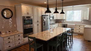 Expansive kitchen featuring a large island with granite countertop, white cabinetry with dark hardware, stainless steel appliances, and wood-finish flooring