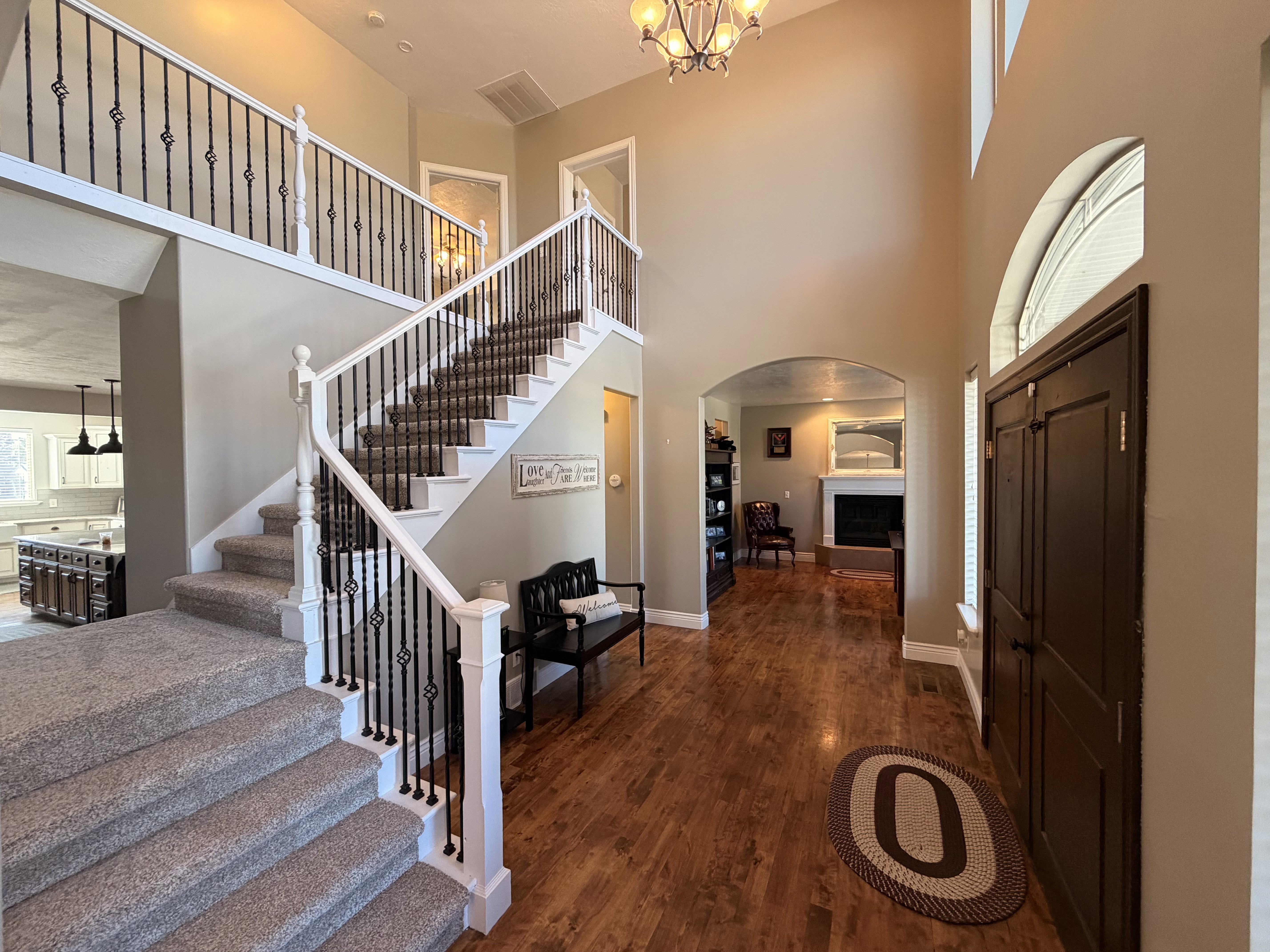 Two-story foyer featuring hardwood flooring, a grand staircase with carpeted treads and wrought iron balusters, and an arched entryway to an interior space with a fireplace