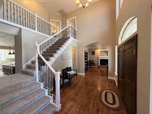 Two-story foyer featuring hardwood flooring, a grand staircase with carpeted treads and wrought iron balusters, and an arched entryway to an interior space with a fireplace