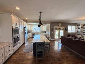 Spacious kitchen featuring extensive white cabinetry, a large center island with pendant lighting, and stainless steel double ovens