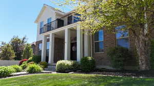 Brick and stucco exterior featuring a columned front porch, second-story balcony with iron railing, and a mature tree providing natural shade