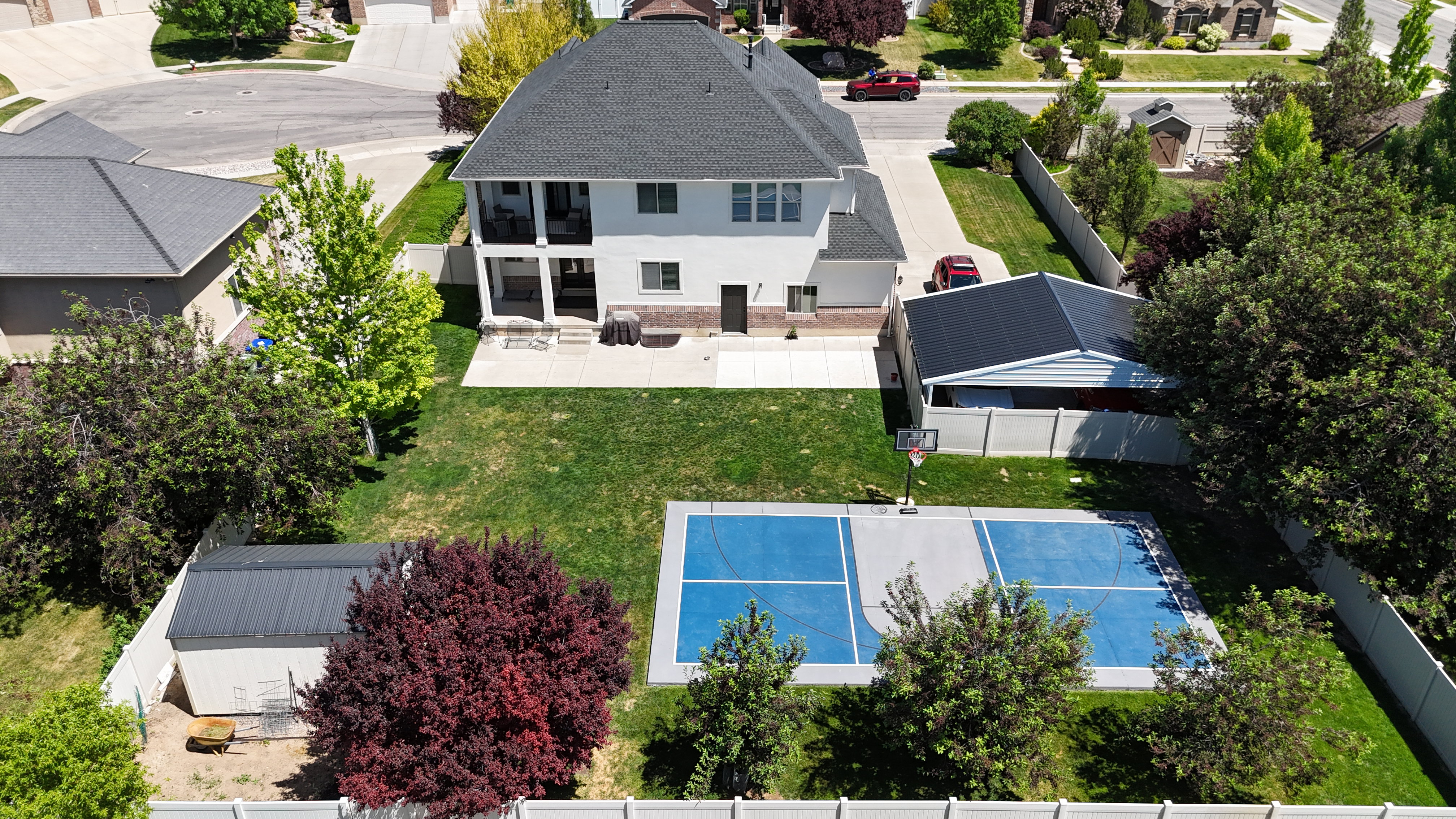 Expansive backyard featuring a multi-sport court with blue surfacing, a dedicated storage shed, mature trees, and a spacious rear patio