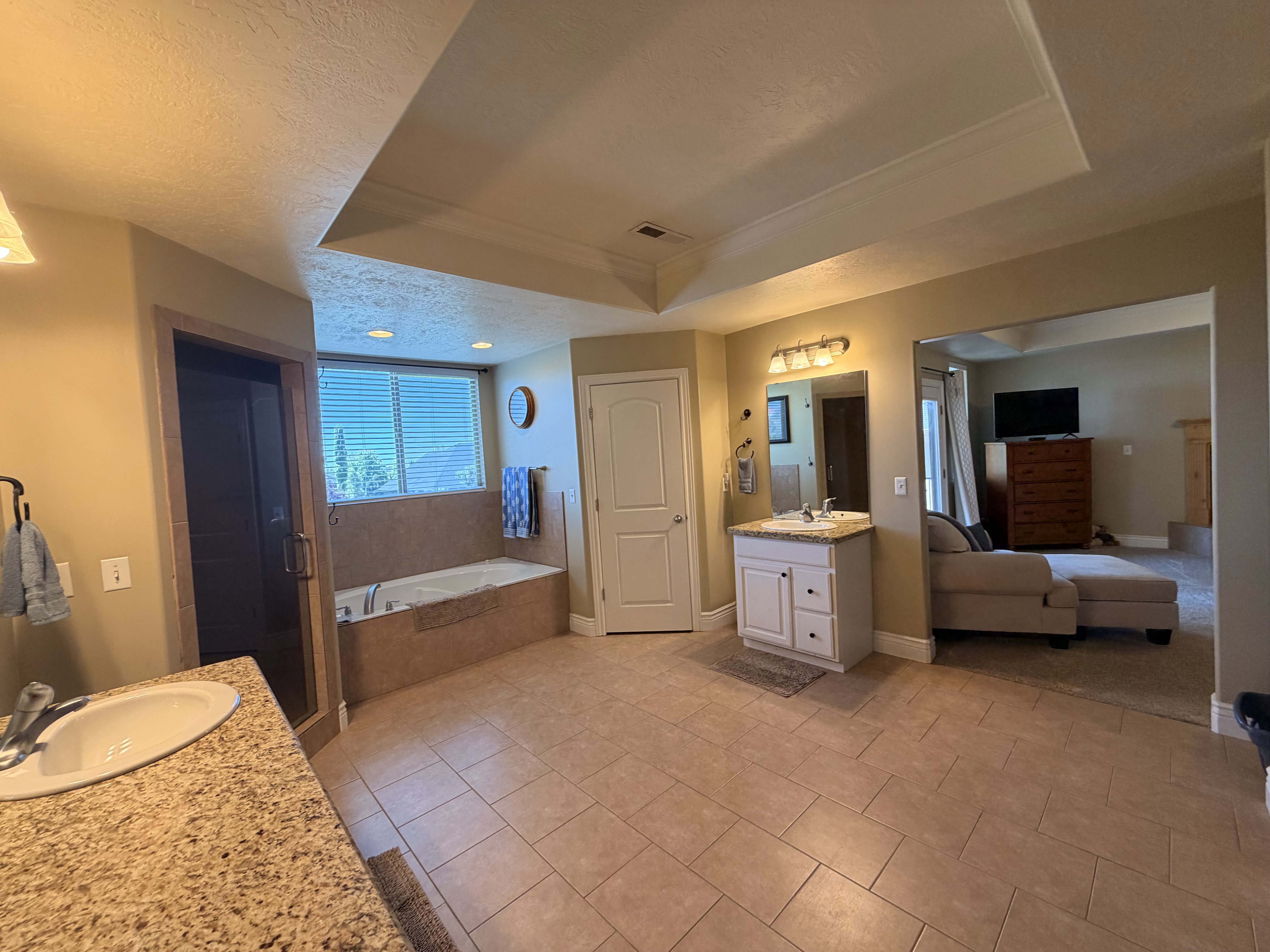 Spacious bathroom featuring a large soaking tub, separate shower enclosure, dual vanity areas with granite-finish countertops, and rectangular floor tiling