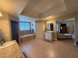 Spacious bathroom featuring a large soaking tub, separate shower enclosure, dual vanity areas with granite-finish countertops, and rectangular floor tiling