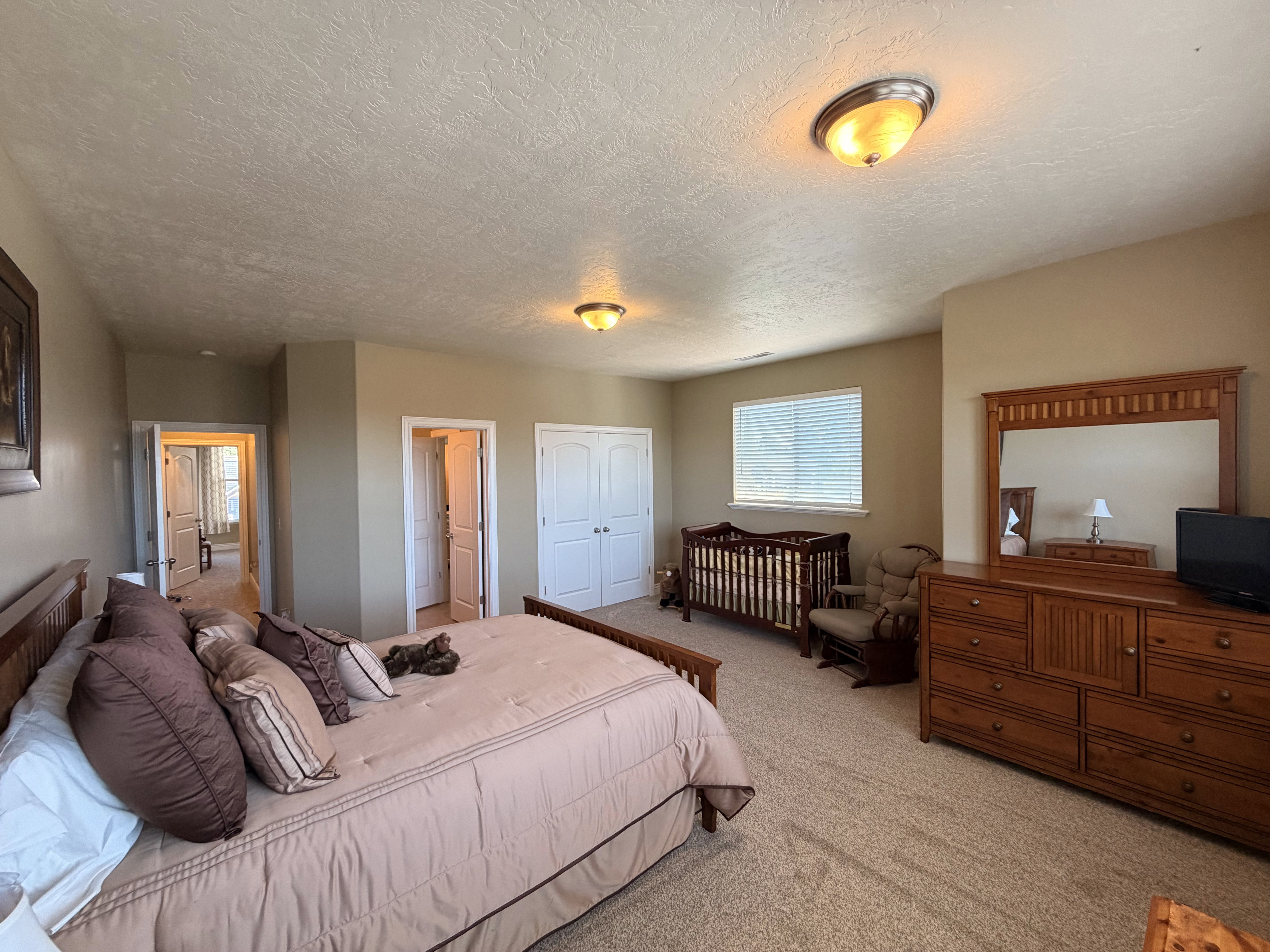 Spacious carpeted room featuring a window with blinds, dual bi-fold closet doors, and two interior doorways