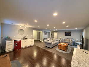 Spacious lower-level living area featuring recessed lighting, a wet bar with white cabinetry and stone-finish countertops, wood-finish flooring, and soft gray wall tones