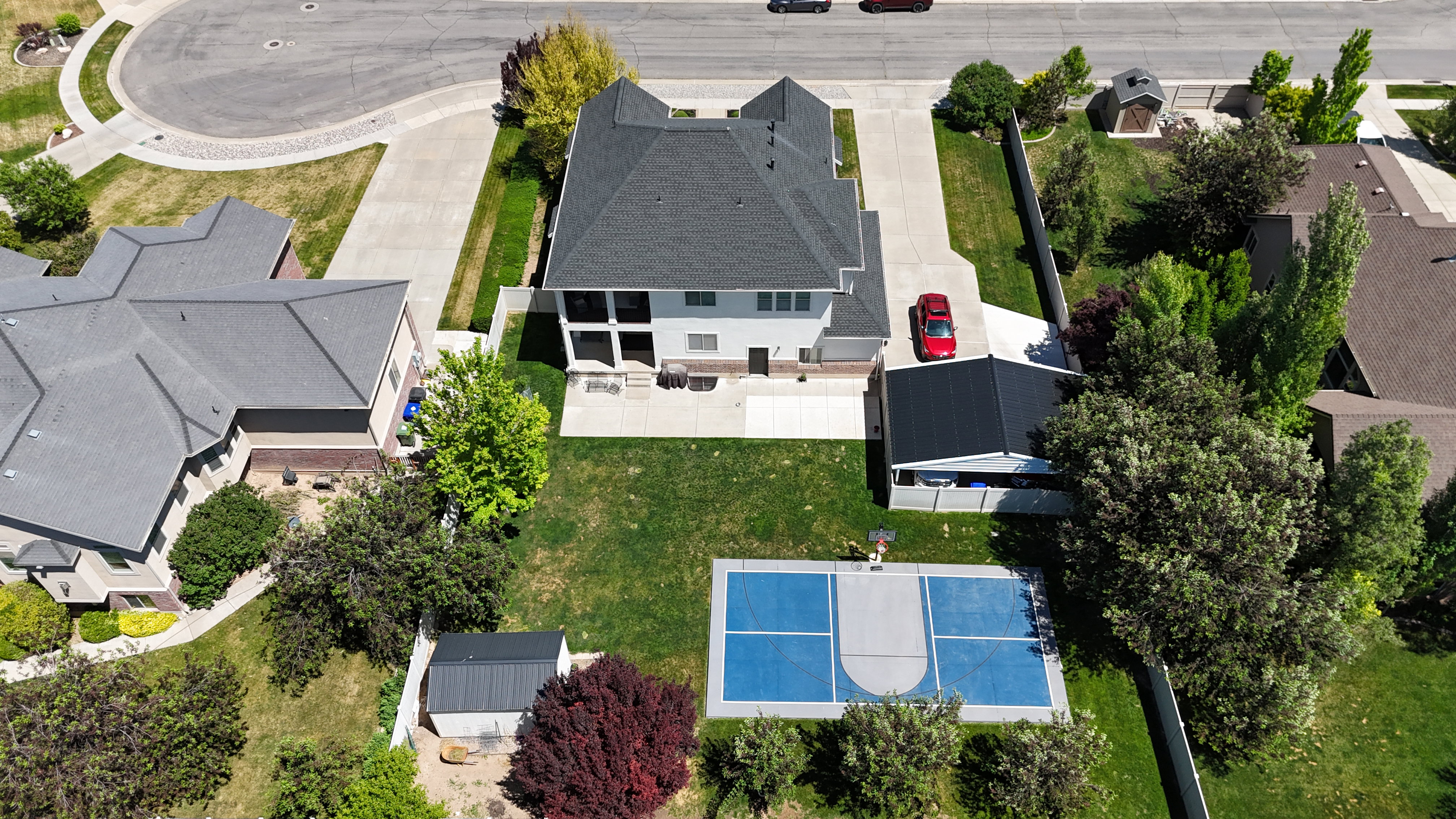 Expansive backyard featuring a blue-surfaced sports court, a manicured lawn, and mature trees