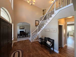 Two-story foyer featuring wood-finish flooring, a grand staircase with wrought iron balusters, an arched entry door with transom window, and an overhead chandelier