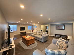 Expansive living area featuring recessed lighting, a stone-clad fireplace with a dark wood mantel, and wood-finish flooring extending to a built-in wet bar