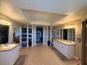 Dual vanity bathroom featuring granite countertops, white cabinetry, tile flooring, and a tray ceiling