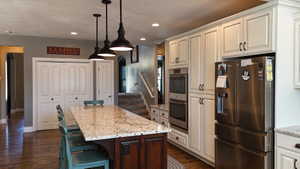 Kitchen featuring a substantial island with a light-toned countertop, wood-finish flooring, recessed lighting, and pendant fixtures
