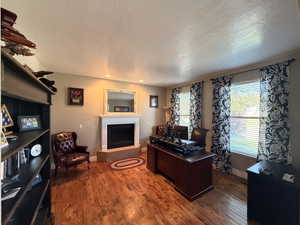 Spacious room featuring hardwood flooring, a corner fireplace with a white mantel, recessed lighting, and multiple windows