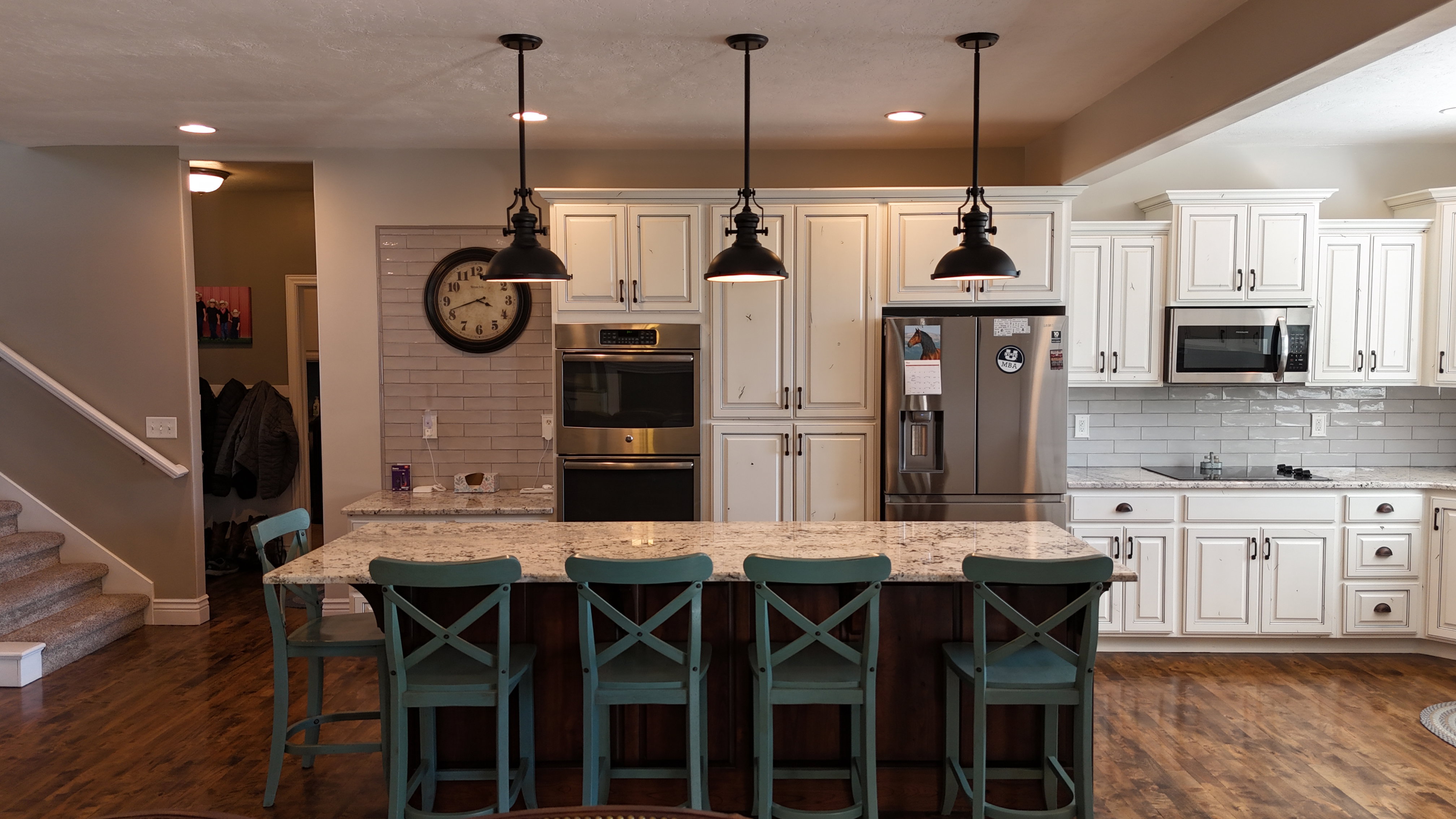 Spacious kitchen featuring an expansive center island with a granite countertop, white shaker cabinetry, stainless steel appliances, and wood-finish flooring