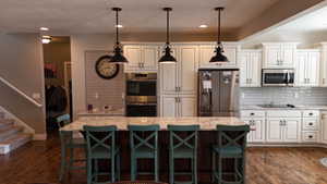 Spacious kitchen featuring an expansive center island with a granite countertop, white shaker cabinetry, stainless steel appliances, and wood-finish flooring
