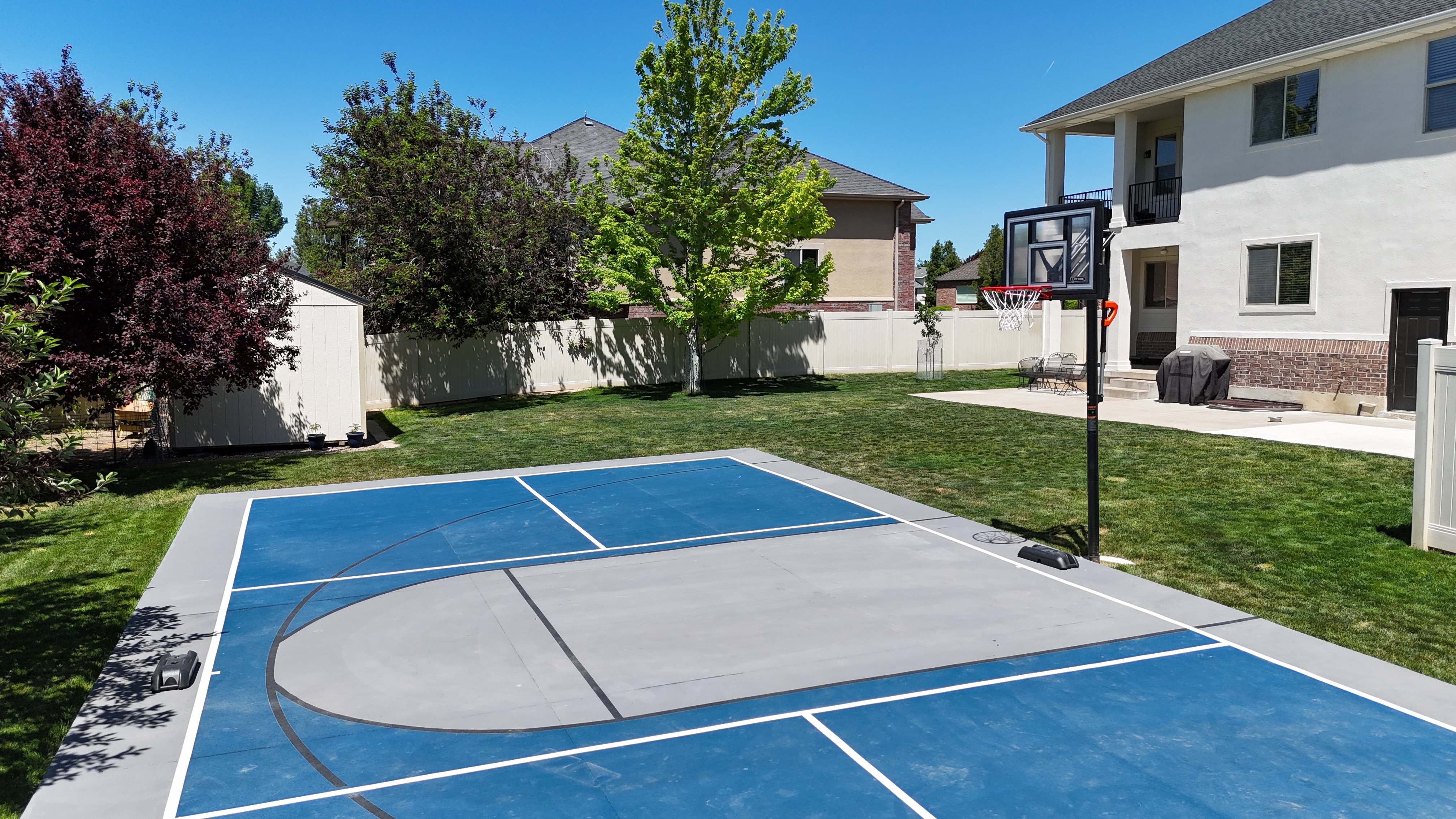 Backyard featuring a sports court with blue and gray surfacing, a basketball hoop, and a privacy fence