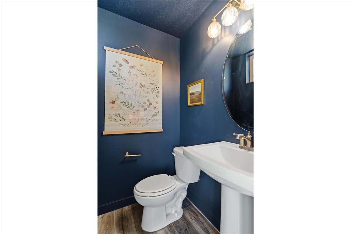 Pedestal sink with brushed nickel faucet, round mirror, and a three-light vanity fixture