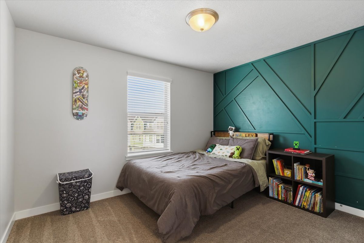 Bedroom featuring a teal geometric accent wall, neutral carpeting, and a single window with blinds