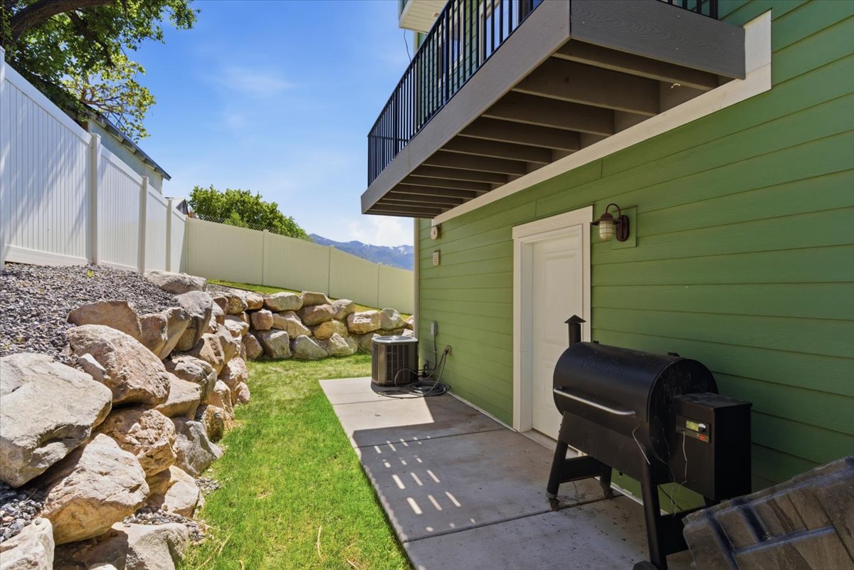 Backyard patio featuring green siding, a white privacy fence, and a rock retaining wall