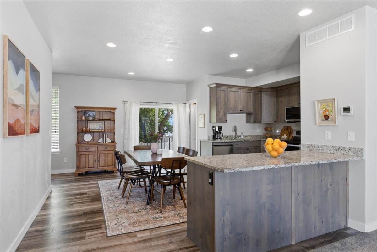 Open-concept living area with wood-finish flooring, recessed lighting, and a modern kitchen featuring wood-finish cabinetry, stainless steel appliances, and granite countertops