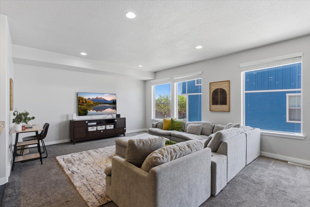 Spacious living area featuring light gray walls, recessed lighting, and multiple windows with white blinds