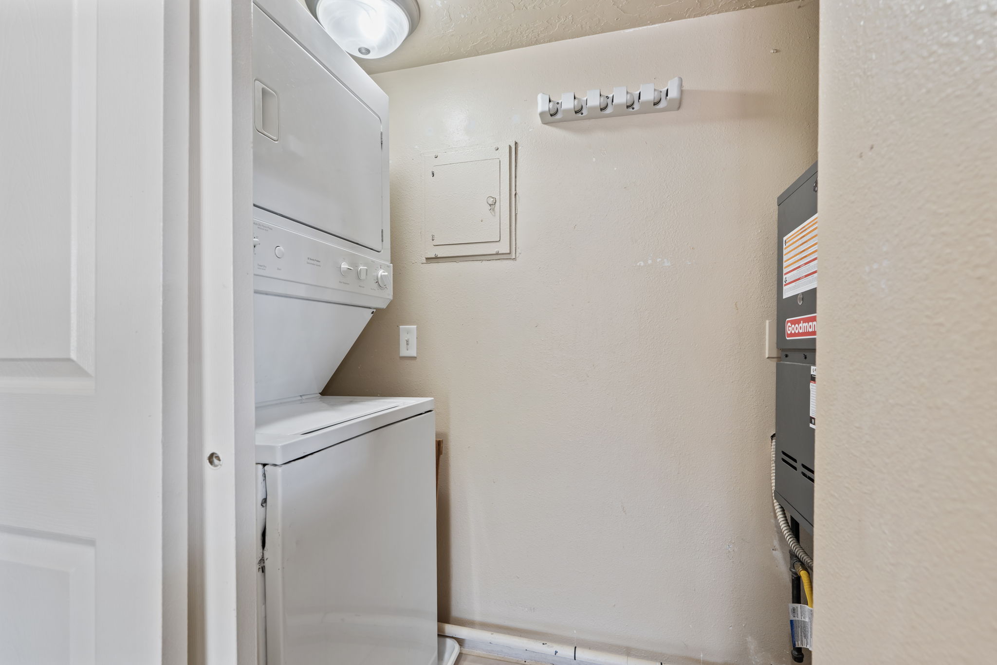 Dedicated laundry area featuring a stacked washer and dryer, ceiling-mounted light fixture, and wall-mounted utility hooks