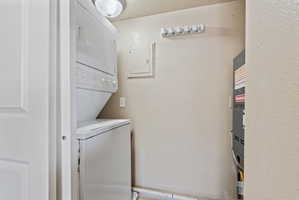 Dedicated laundry area featuring a stacked washer and dryer, ceiling-mounted light fixture, and wall-mounted utility hooks