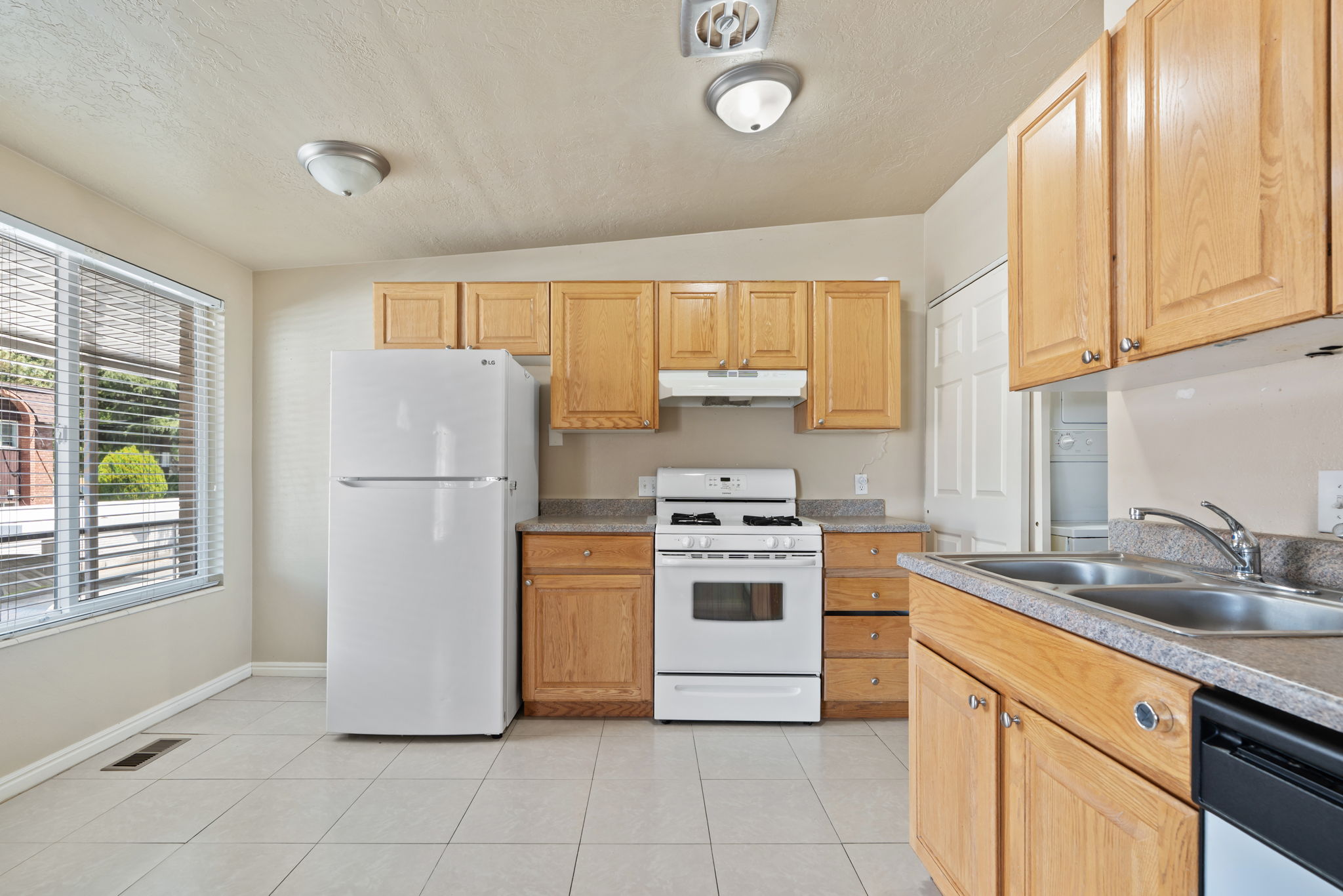 Kitchen featuring wood-finish cabinetry, a double basin stainless steel sink, tile flooring, and a window with blinds