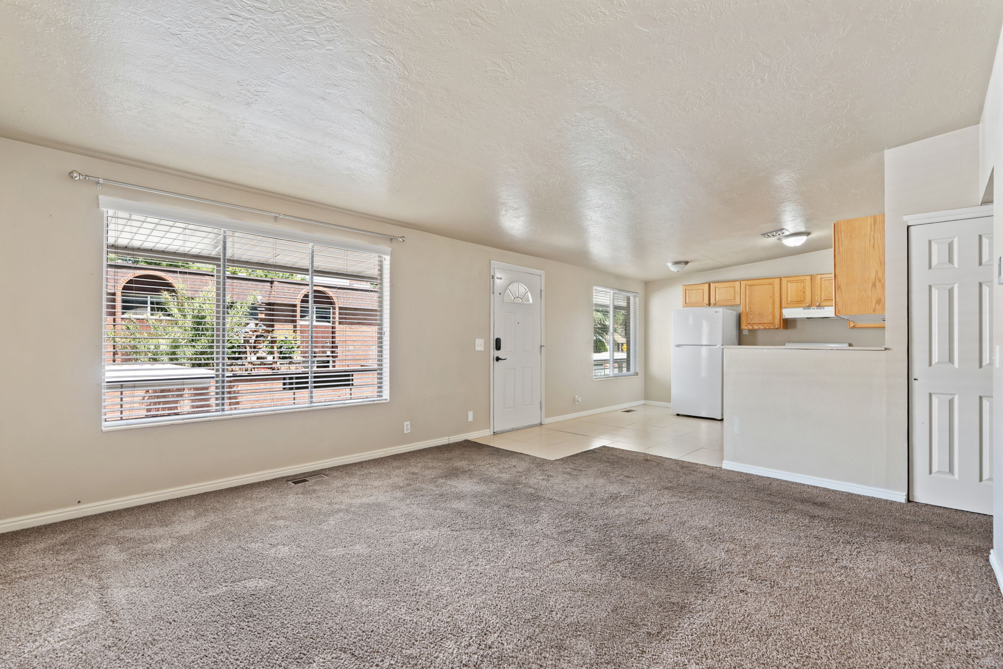 Open-concept living space featuring neutral-toned carpeting, a large window with blinds, and white trim