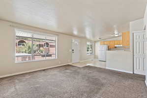 Open-concept living space featuring neutral-toned carpeting, a large window with blinds, and white trim