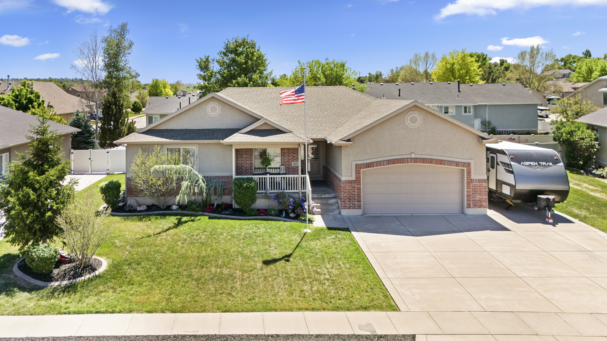 Single-story residence featuring a two-car garage, brick facade detailing, a covered porch, and mature landscaping