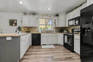 Kitchen featuring wood-finish flooring, white cabinetry, a built-in microwave, a gas range, and a breakfast bar with a light-toned countertop
