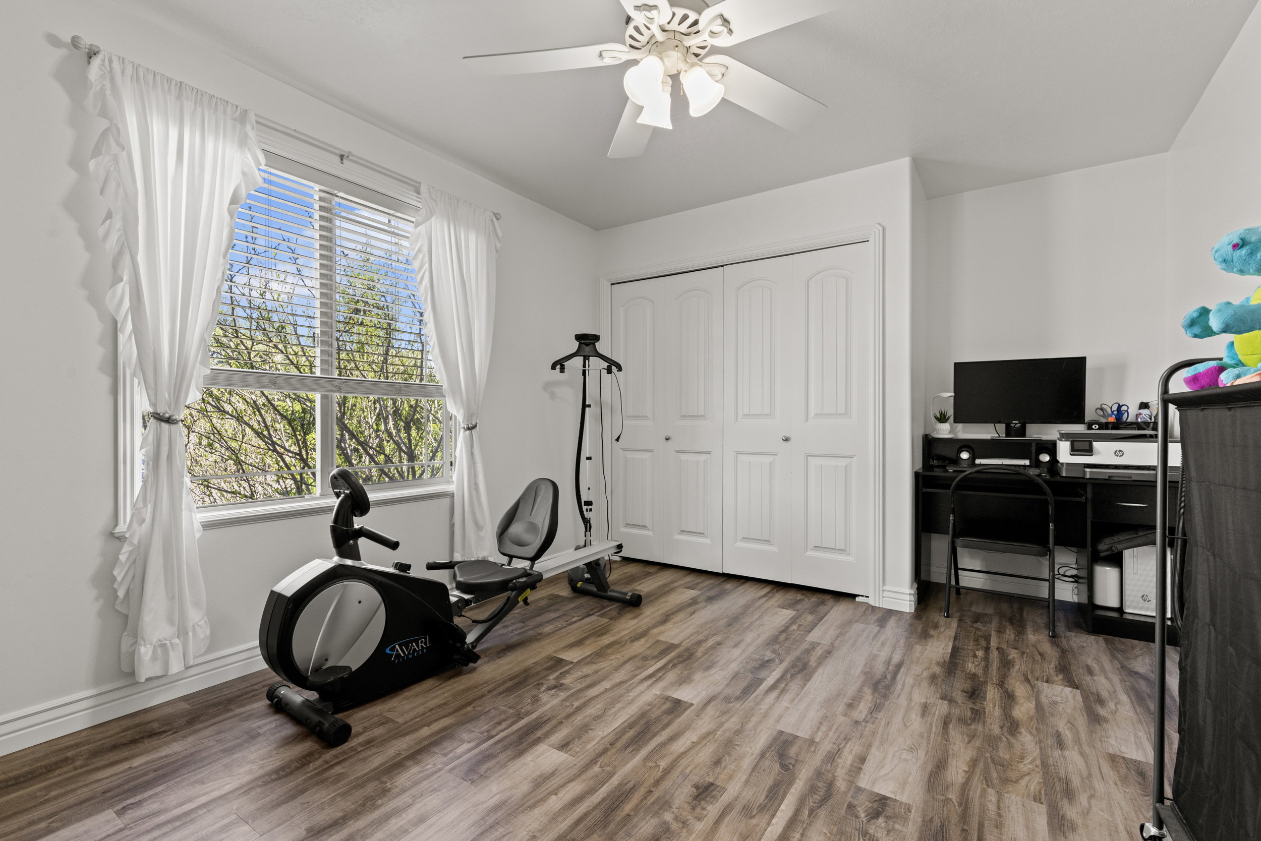 Spacious room featuring wood-finish flooring, a ceiling fan, and a large window with blinds