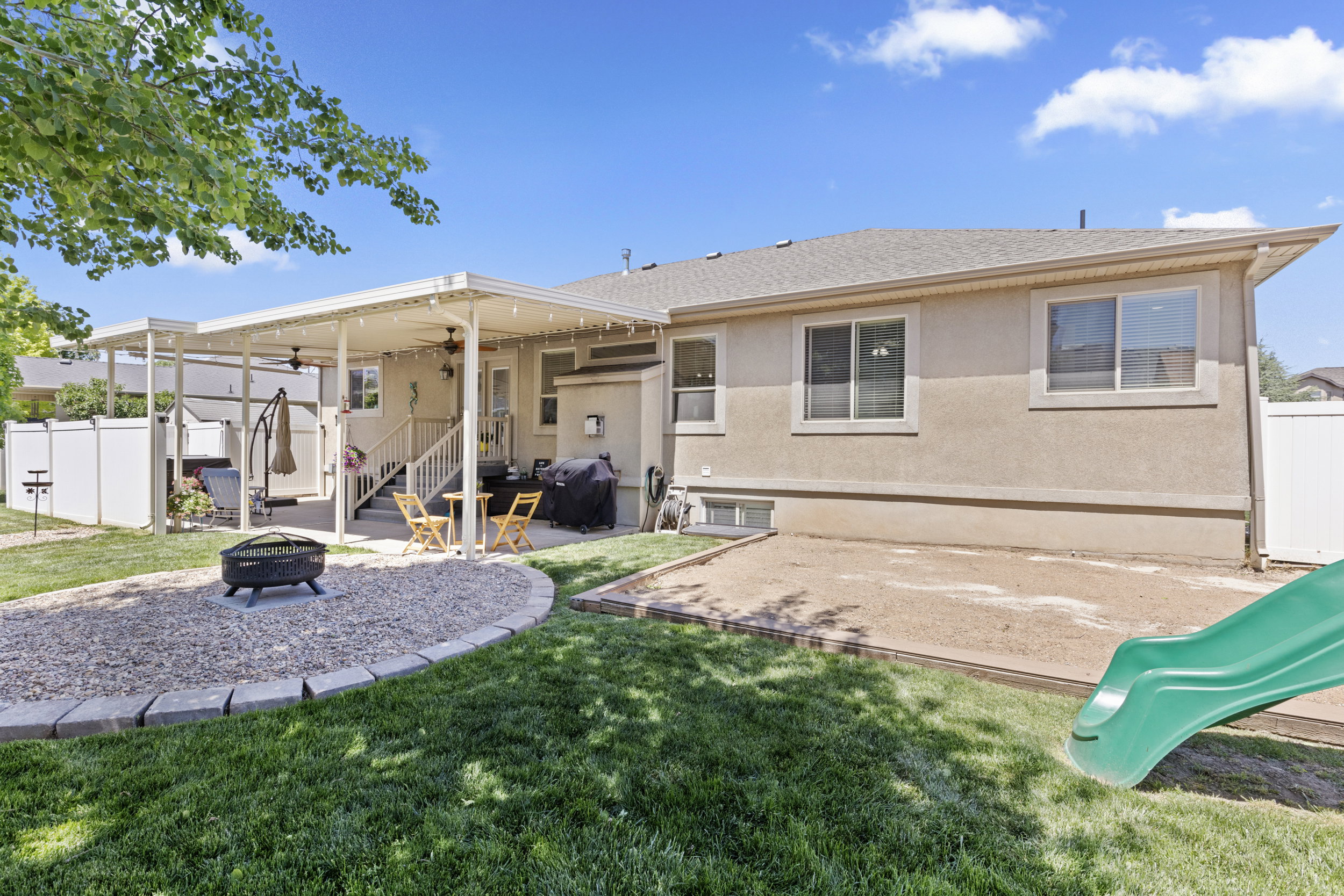 Expansive backyard featuring a covered patio, tiered deck, gravel fire pit area, and a green lawn with a privacy fence