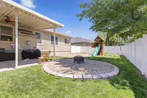 Expansive backyard featuring a covered patio, a defined gravel fire pit area with stone edging, established lawn, and white privacy fencing