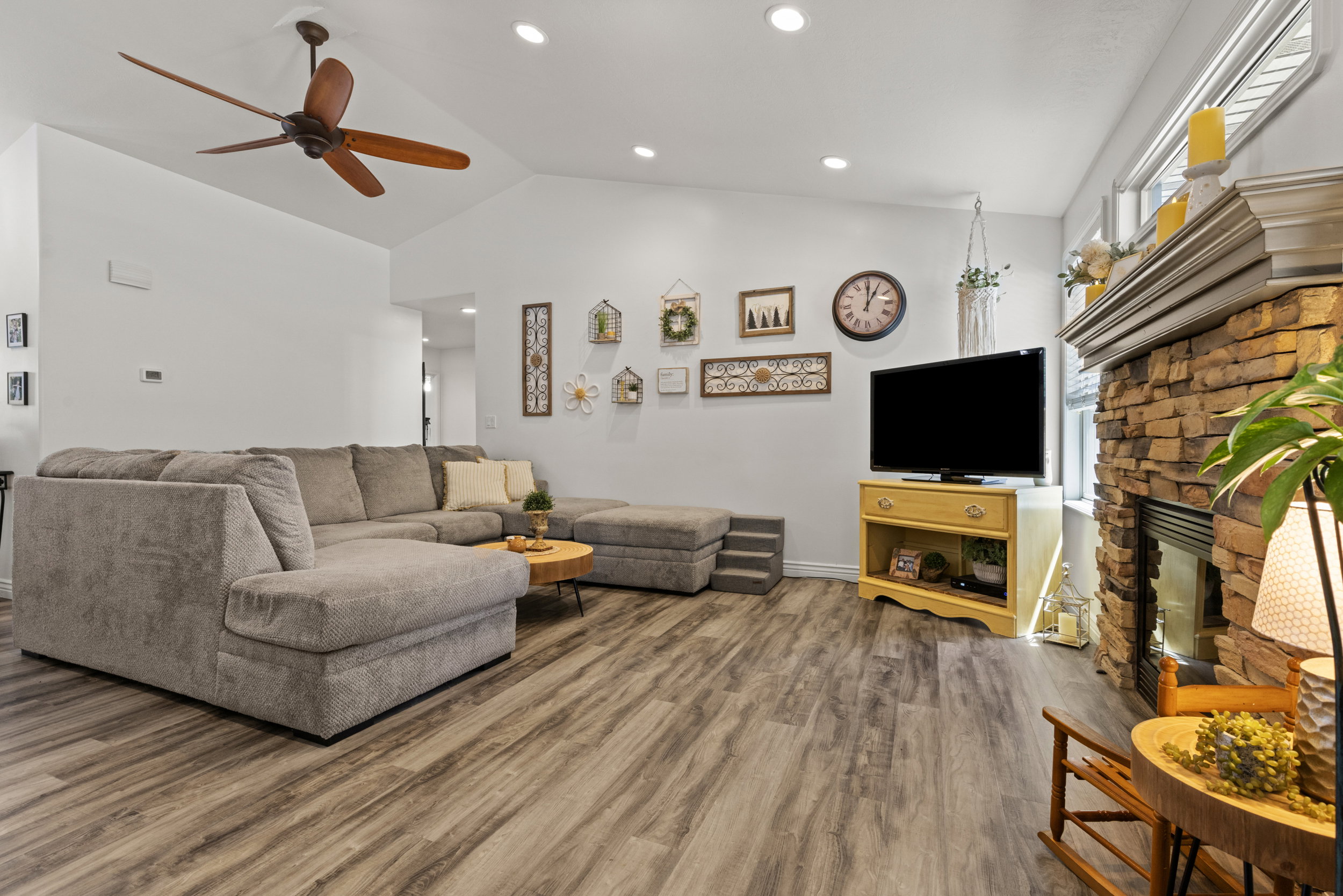 Living area featuring vaulted ceilings with recessed lighting, wood-finish flooring, and a stone-faced fireplace