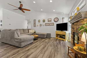 Living area featuring vaulted ceilings with recessed lighting, wood-finish flooring, and a stone-faced fireplace